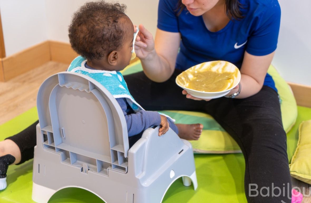 Une pro en crèche qui donne à manger à un enfant