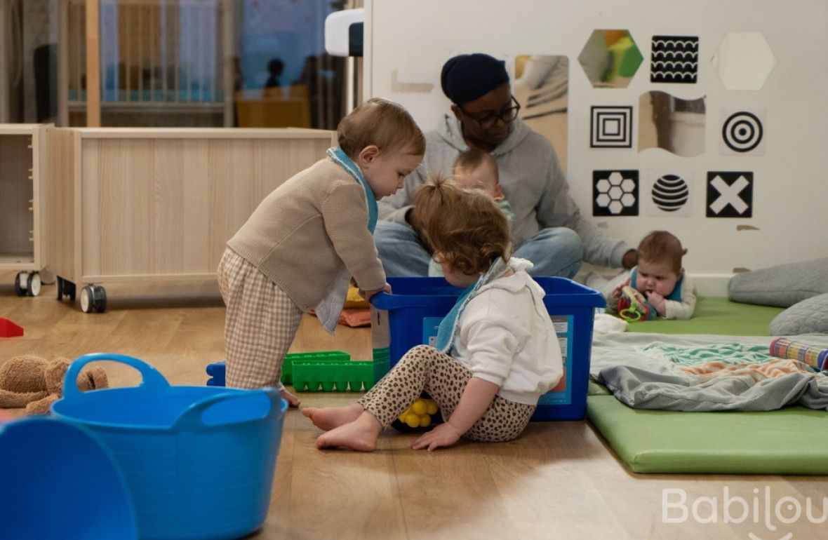 Une professionnelle en crèche assise entouré de trois d'enfants 