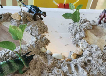 Une mise en scène avec des jouets dinosaures dans un décor avec des pierres et du sable 